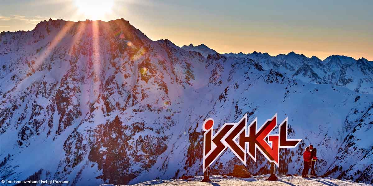 Winterliche Landschaft bei Sonnenaufgang mit Paar neben Ischgl-Schriftzug